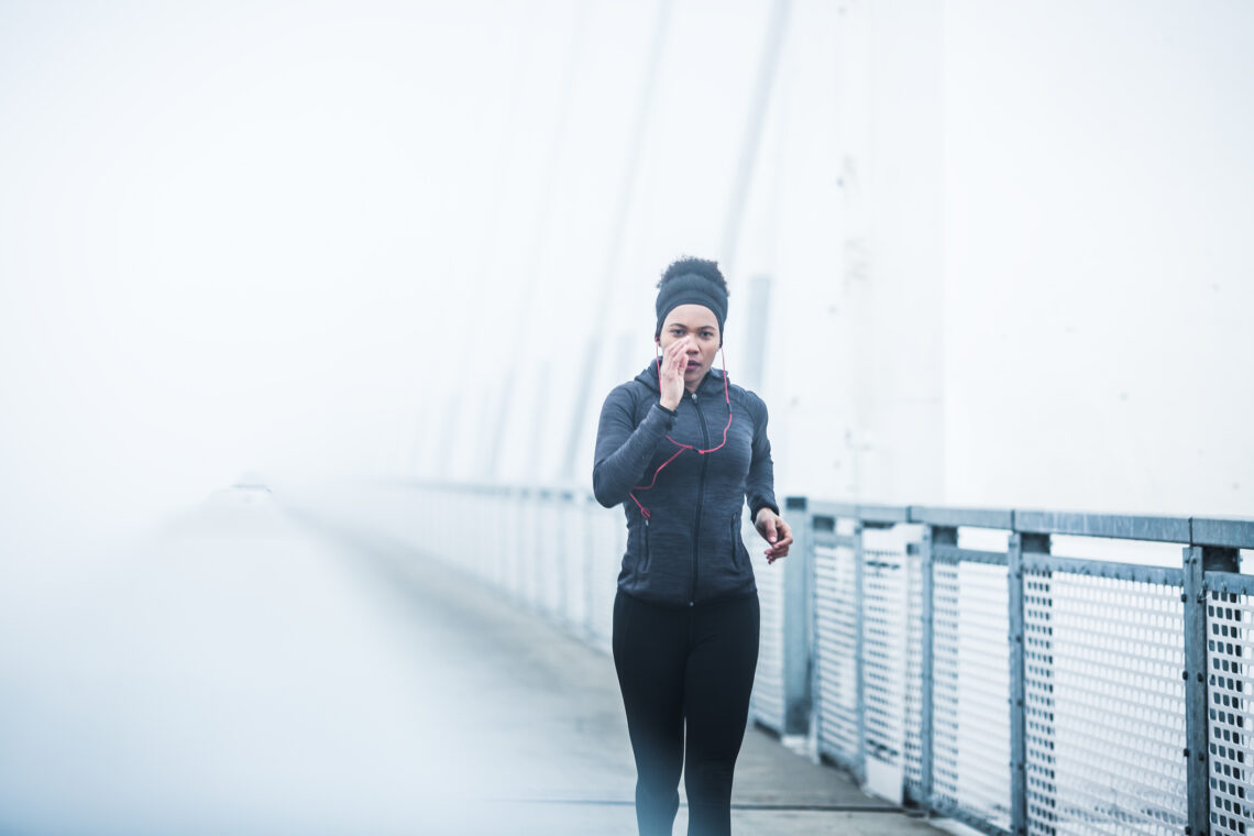 Žena trči preko mosta po maglovitom danu.